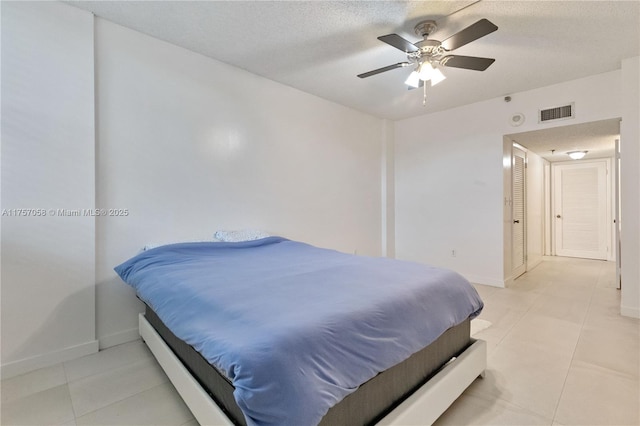 bedroom featuring light tile patterned floors, visible vents, baseboards, a ceiling fan, and a textured ceiling