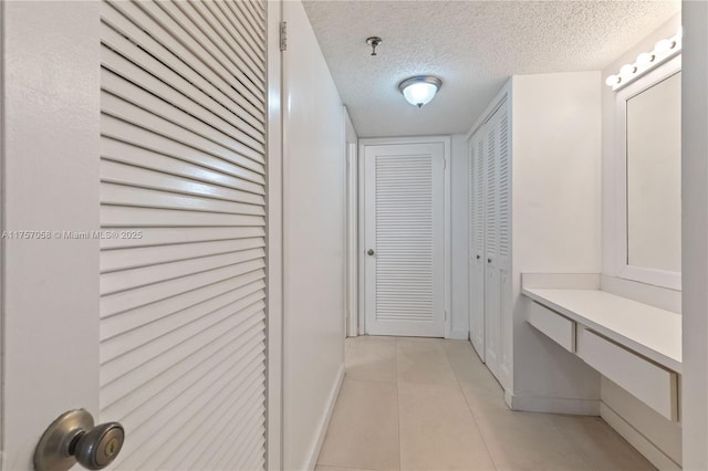 hall with light tile patterned floors, baseboards, and a textured ceiling