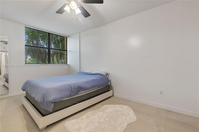 bedroom featuring a textured ceiling, light tile patterned floors, a ceiling fan, and baseboards