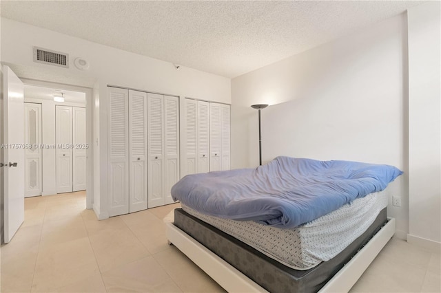 bedroom with a textured ceiling, visible vents, multiple closets, and tile patterned floors