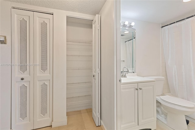 bathroom featuring a closet, toilet, vanity, a textured ceiling, and tile patterned flooring