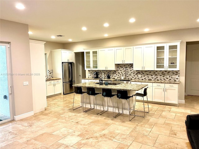 kitchen with an island with sink, backsplash, a sink, and freestanding refrigerator