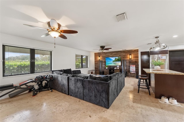 living room with ceiling fan, wooden walls, and visible vents