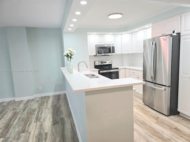 kitchen featuring light wood finished floors, light stone countertops, stainless steel appliances, white cabinetry, and a sink