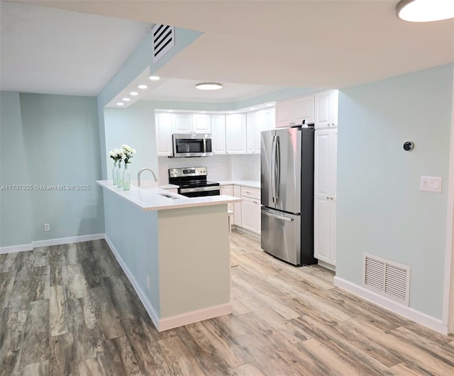 kitchen with a peninsula, appliances with stainless steel finishes, a sink, and visible vents