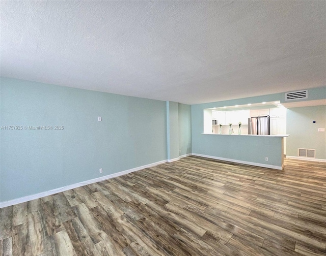 empty room with dark wood-type flooring, visible vents, a textured ceiling, and baseboards