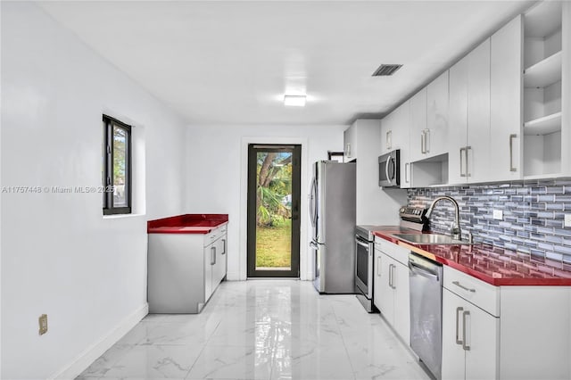 kitchen featuring stainless steel appliances, a sink, marble finish floor, decorative backsplash, and dark countertops