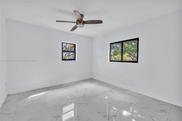 unfurnished room with marble finish floor, plenty of natural light, and baseboards