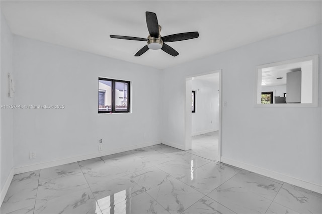 spare room featuring ceiling fan, marble finish floor, and baseboards