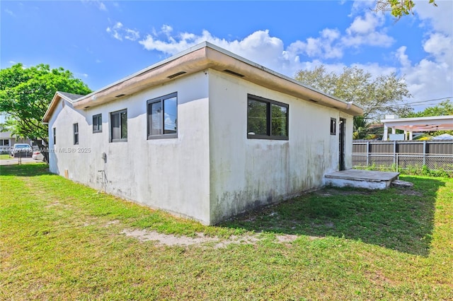 view of side of property featuring stucco siding, a lawn, and fence