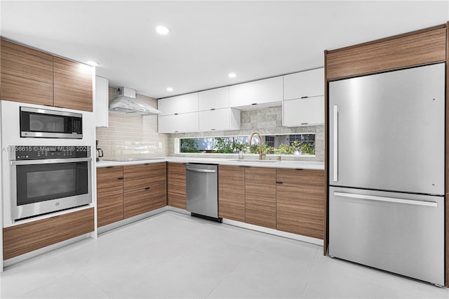 kitchen featuring a sink, light countertops, appliances with stainless steel finishes, and wall chimney range hood