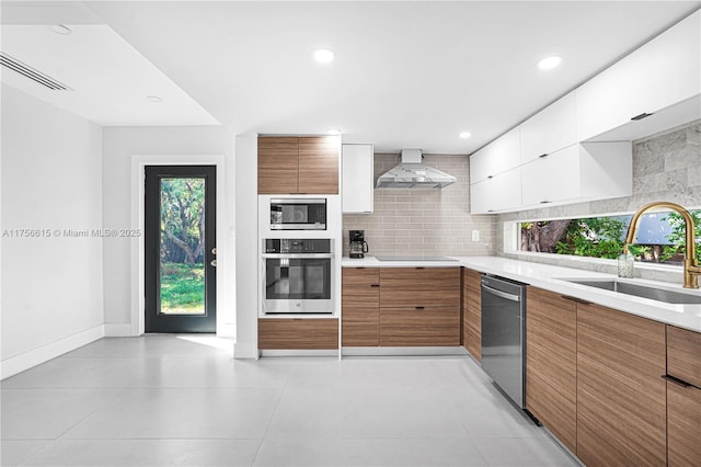 kitchen featuring stainless steel appliances, a sink, decorative backsplash, wall chimney exhaust hood, and modern cabinets