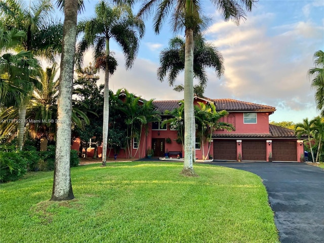 mediterranean / spanish-style home with stucco siding, aphalt driveway, a front yard, a garage, and a tiled roof