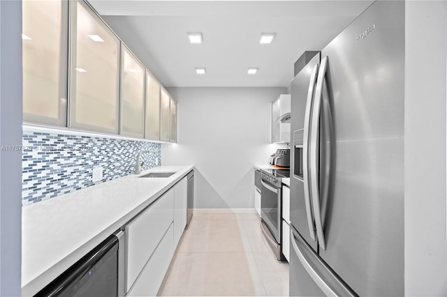 kitchen with light tile patterned floors, stainless steel appliances, light countertops, backsplash, and a sink