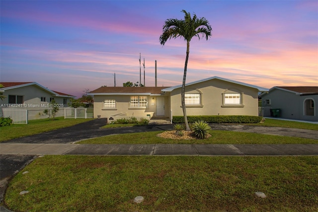 ranch-style house with aphalt driveway, a lawn, fence, and stucco siding