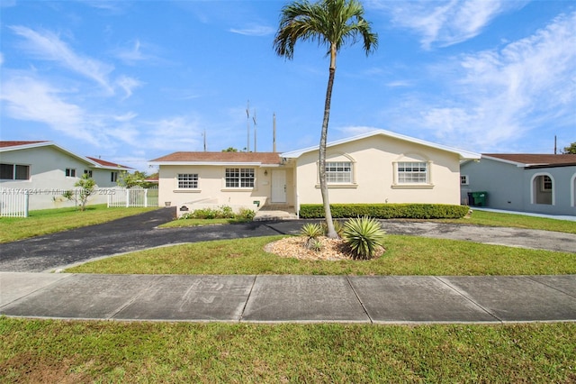 ranch-style house with driveway, stucco siding, fence, and a front yard