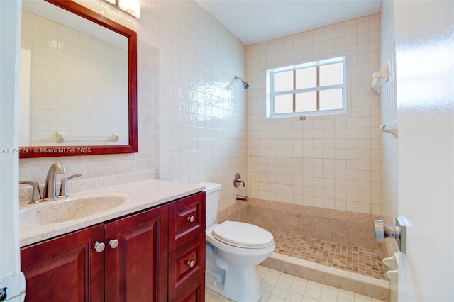 bathroom with toilet, tile walls, vanity, a tile shower, and tile patterned floors