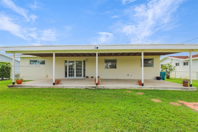 rear view of property featuring a yard, french doors, a patio, and stucco siding