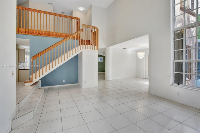 unfurnished living room featuring a high ceiling, stairway, an inviting chandelier, and tile patterned floors