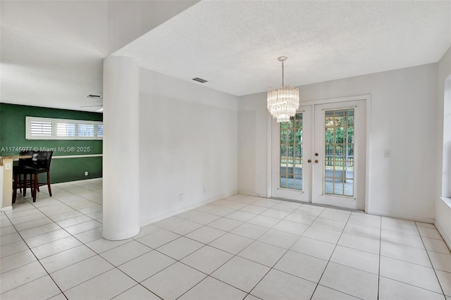 tiled spare room with a textured ceiling, a notable chandelier, visible vents, and a healthy amount of sunlight