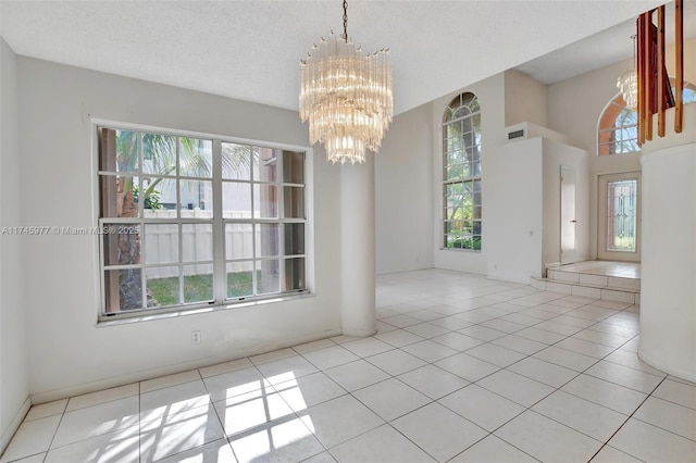 tiled spare room with an inviting chandelier, visible vents, and a textured ceiling