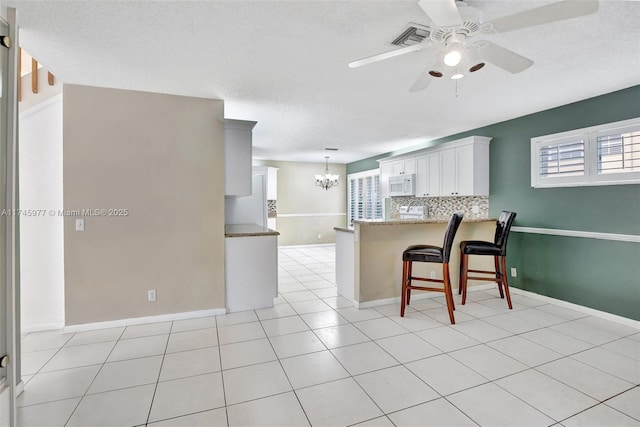 kitchen with tasteful backsplash, white microwave, a kitchen bar, white cabinetry, and light tile patterned flooring