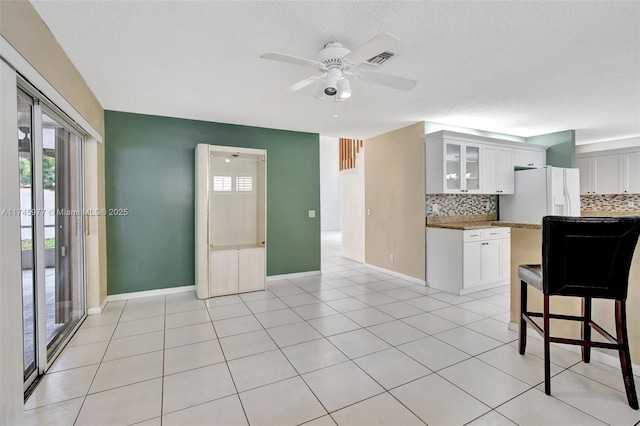 kitchen featuring tasteful backsplash, white refrigerator with ice dispenser, visible vents, white cabinets, and glass insert cabinets