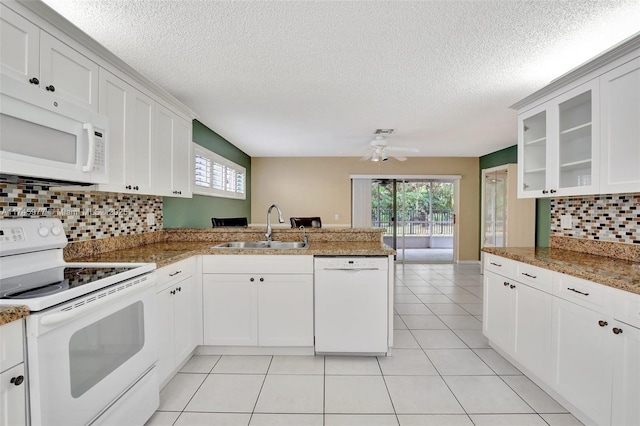 kitchen with light tile patterned floors, a peninsula, white appliances, a sink, and glass insert cabinets