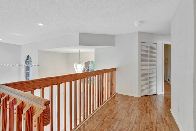 hall featuring a textured ceiling, recessed lighting, a notable chandelier, wood finished floors, and baseboards