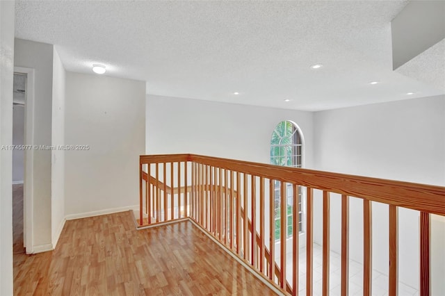 hall with a textured ceiling, baseboards, wood finished floors, and recessed lighting