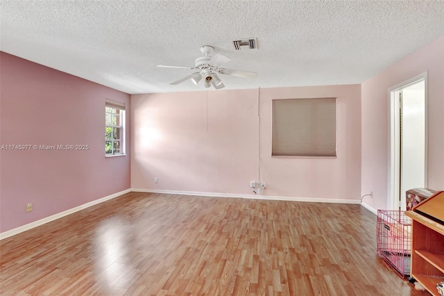 spare room featuring ceiling fan, a textured ceiling, wood finished floors, visible vents, and baseboards