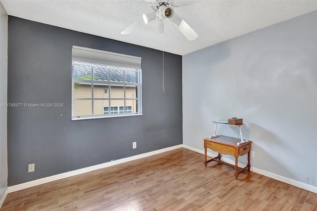 spare room with ceiling fan, a textured ceiling, baseboards, and wood finished floors