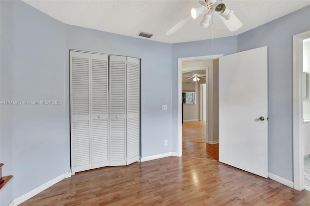 unfurnished bedroom with light wood finished floors, baseboards, visible vents, a textured ceiling, and a closet