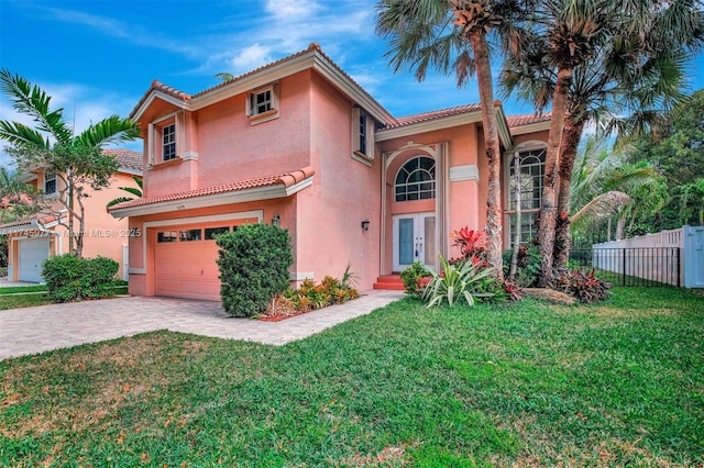 mediterranean / spanish-style home with decorative driveway, stucco siding, fence, a garage, and a tiled roof