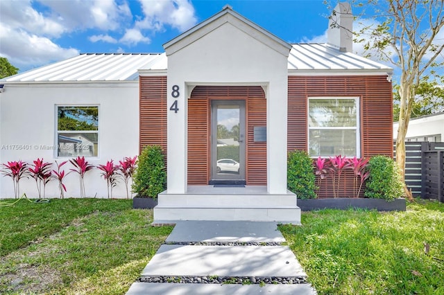 doorway to property with a lawn, a chimney, metal roof, a standing seam roof, and stucco siding