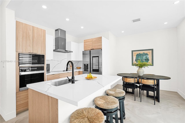 kitchen with appliances with stainless steel finishes, a sink, wall chimney range hood, an island with sink, and modern cabinets