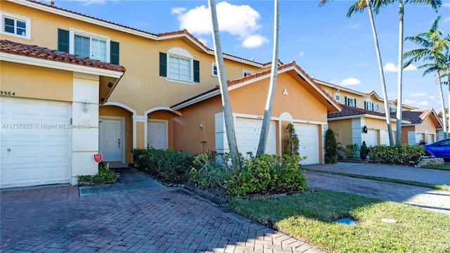 view of front of property featuring a garage, decorative driveway, a tiled roof, and stucco siding