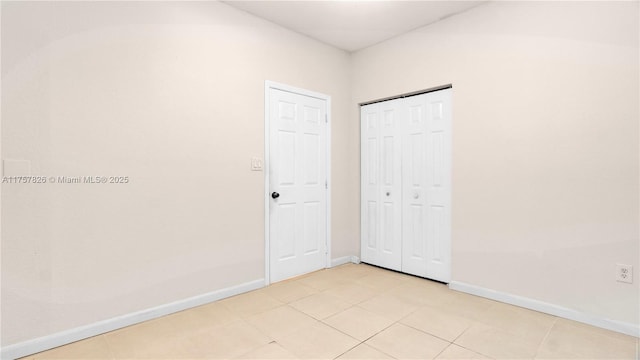 unfurnished bedroom featuring a closet, light tile patterned flooring, and baseboards