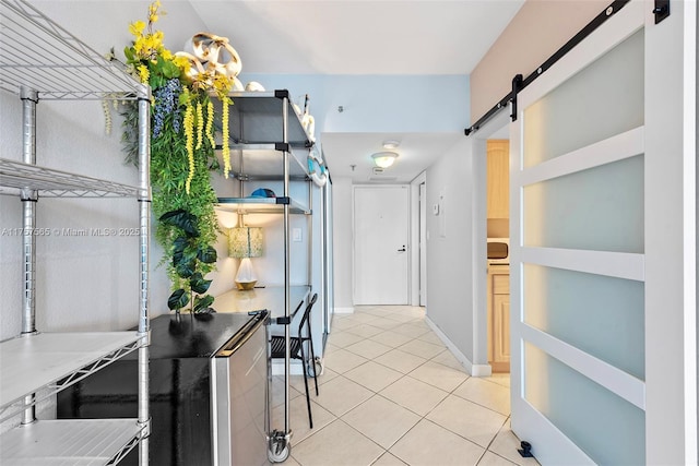 corridor featuring light tile patterned floors, baseboards, and a barn door