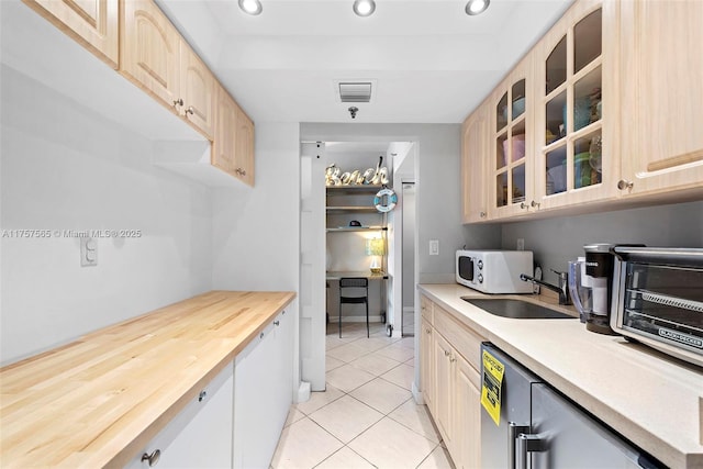 kitchen featuring light tile patterned floors, white microwave, glass insert cabinets, light brown cabinets, and a sink