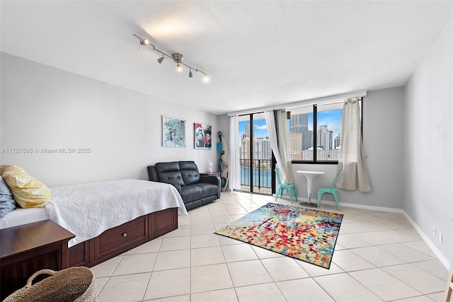 bedroom with access to exterior, a view of city, light tile patterned floors, rail lighting, and baseboards