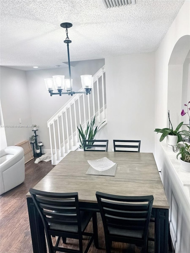 dining room with visible vents, arched walkways, wood finished floors, a textured ceiling, and a chandelier