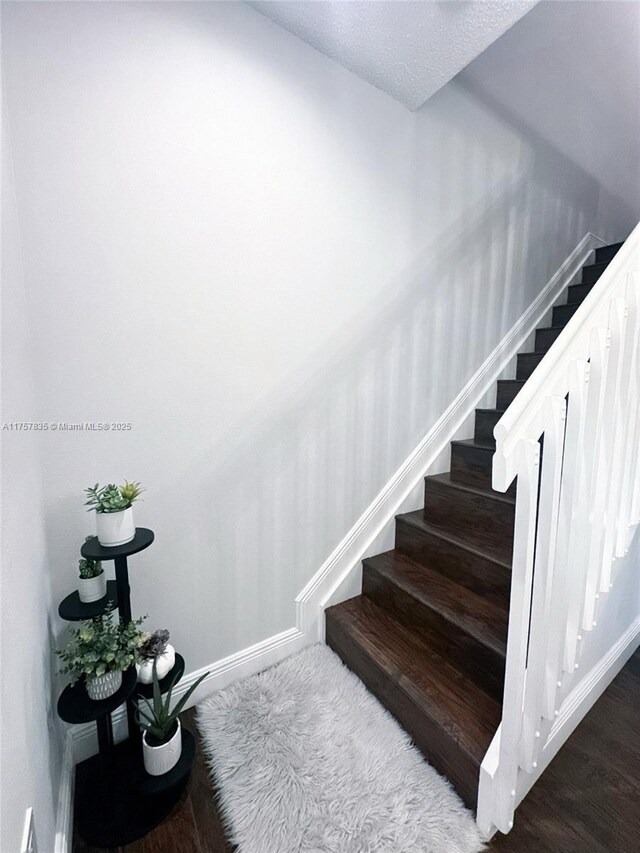 staircase featuring a textured ceiling, baseboards, and wood finished floors