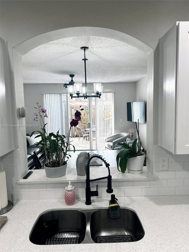 interior details with a textured ceiling, arched walkways, a chandelier, a sink, and decorative light fixtures