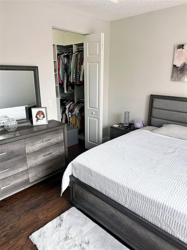 bedroom featuring a textured ceiling, a closet, wood finished floors, and a walk in closet