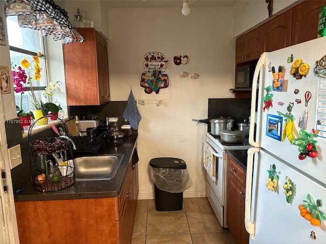 kitchen featuring white appliances, light tile patterned floors, brown cabinetry, dark countertops, and a sink