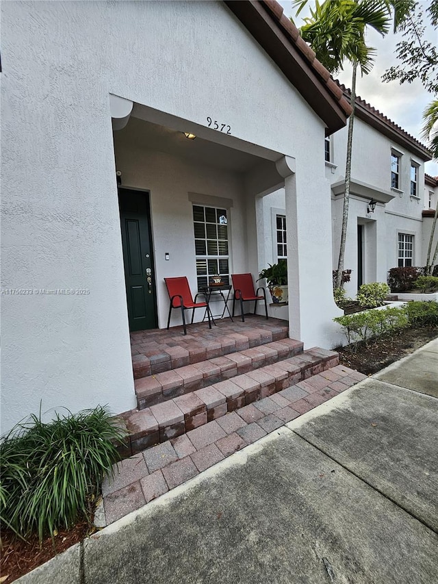 entrance to property with a porch, a tile roof, and stucco siding