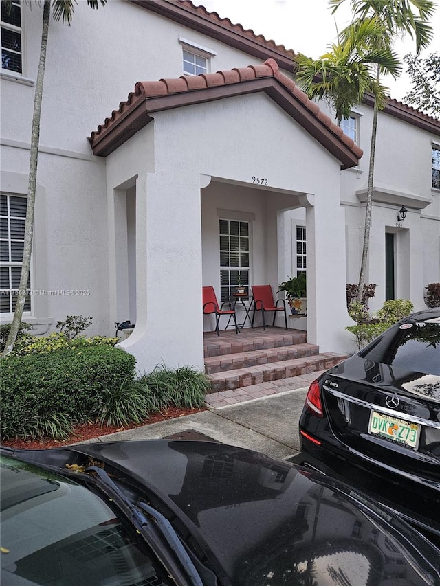 doorway to property featuring covered porch, a tile roof, and stucco siding