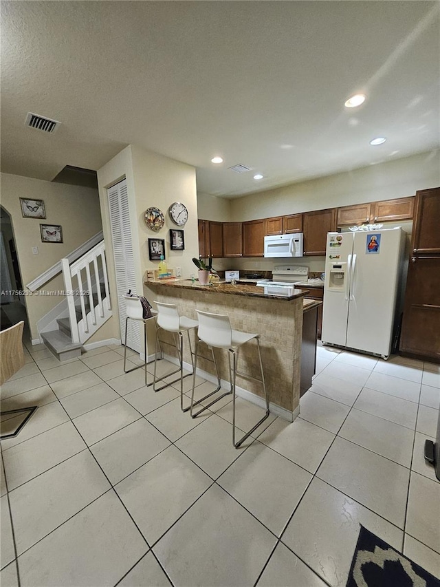 kitchen with white appliances, light tile patterned floors, visible vents, a peninsula, and a kitchen bar