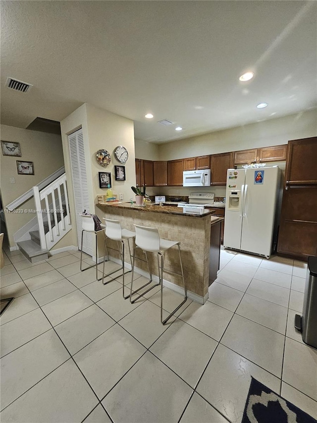 kitchen with light tile patterned floors, a peninsula, white appliances, visible vents, and a kitchen breakfast bar